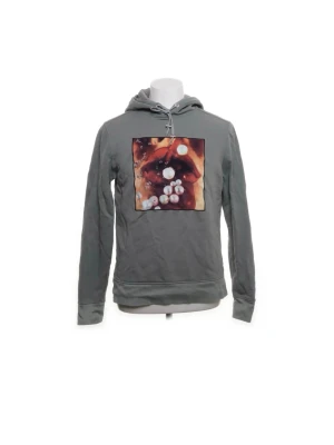 Grå Limitato Hoodie - Snygg grå Limitato Hoodie med huva och dragsko. På bröstet finns ett grafiskt tryck med motiv av läppar och pärlor i starka färger. Hoodien har långa ärmar och ribbade muddar. Perfekt för dig som vill sticka ut med en unik detalj. Materialet känns mjukt och bekvämt.