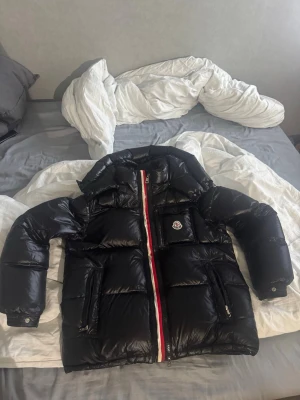 Svart Moncler dunjacka med röd/vit dragkedja - Säljer nu min Moncler montebiliard jacka, den är i bra skick och är hyfsat unik. Skriv DM vid fler frågor:)