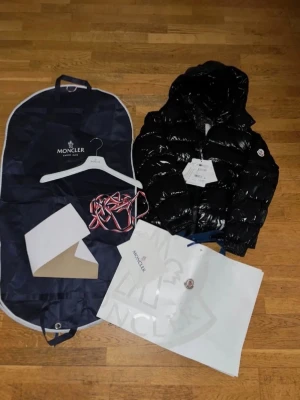 Svart glansig dunjacka från Moncler - Säljer min Moncler maya då den är för liten för mig. Endast använd fåtal gånger så den är i stort sätt nyskick och alla äktighetsbevis skickas med.                 Pris är diskuterbart.                                                              Storlek:2