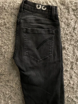 Mörkgråa jeans från Dondup - Säljer ett par mörkgråa jeans från Dondup, tillverkade i Italien. Jeansen har klassisk femficksdesign, diskret D-detalj på bakfickan och OG-tryck i midjan. Materialet är mjukt jeans-tyg med en mörk tvätt som ger en clean look. Kan gå ner lite i pris vid snabb affär.