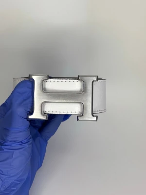 Vit H-skärp med metallspänne - Snyggt vitt skärp i skinn med ett stort, borstat metallspänne i form av ett H. Skärpet har svart kant och diskreta sömmar längs kanterna. Perfekt accessoar för att lyfta vilken outfit som helst.