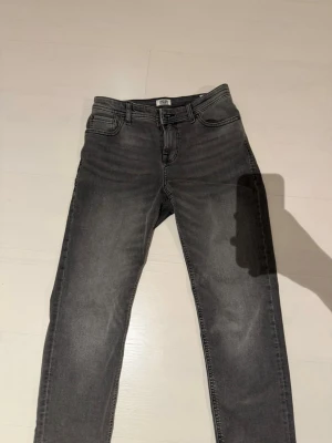 Grå jeans med rak passform - Säljer just nu mina Jack and Jones jeans i modellen regular Cales då dem är lite mer vida i stilen. Storleken är 13y eller 158 cm men den passar även längre! Jeansen är ljus gråa med svarta sömmar! Säljer dem för att jag har vuxit ur dem!