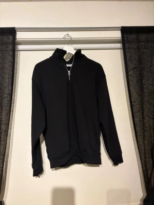 Svart halvzip sweatshirt  - Svart sweatshirt med halv dragkedja och hög krage. Tröjan har en avslappnad passform, långa ärmar och ribbade muddar vid ärmslut och nederkant. Perfekt för en stilren och enkel look.