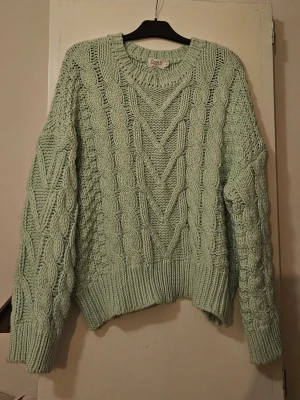 Mintgrön kabelstickad tröja  - Superfin mintgrön kabelstickad tröja från NaKD med chunky struktur och bred ribbad mudd vid ärmslut och nederkant. Tröjan har rund halsringning och ett snyggt mönster med flätor både fram och på ärmarna. Perfekt för dig som gillar oversized och mysig stil.
