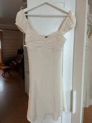 Vit kortklänning med puffärmar - Supersöt vit kortklänning med puffiga kortärmar och rynkade detaljer över bysten. Klänningen har en lätt utsvängd kjol och är tillverkad i ett tunt, strukturerat tyg som ger en luftig känsla. Perfekt för varma dagar och somriga tillfällen. Jätteskön, stretchig och luftig. Använd 1-2 gånger bara 🩷