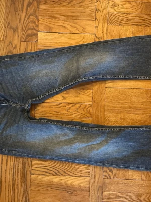 Blå bootcut jeans med slitningar - Säljer ett par klassiska blå jeans med bootcut ben och snygga slitningar på framsidan. Jeansen har två bakfickor och kontrastsömmar. Perfekta till en avslappnad stil och tillverkade i tåligt denimtyg.