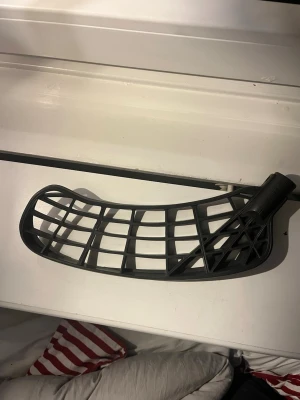 Svart innebandyblad plast ZONE MAKER BLAD - Säljer ett svart innebandyblad i plast med ett klassiskt rutmönster och böjd form. Perfekt för dig som vill byta blad på din klubba och få bättre bollkontroll. Passar de flesta standardklubbor och är lätt att montera.