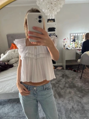 Vit volang topp från Zara - Supersöt vit topp från Zara med breda axelband och flera lager volanger. Toppen är croppad och har en luftig, plisserad design som ger en romantisk vibe. Perfekt till jeans eller kjol för en trendig look. Slutsåld💗