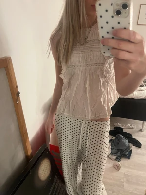 Vit ärmlös blus med volangdetaljer - Söt vit blus från Hollister med volangdetaljer längs axlarna och spetsinslag framtill. Blusen är ärmlös och har en lätt rynkad struktur samt rund halsringning. Perfekt för en fräsch och somrig look.