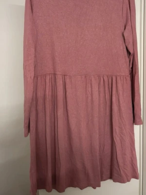 Rosa långärmad klänning  - En enkel och skön rosa klänning med lång ärm och rund hals. Klänningen har en lös passform med rynkad midja som ger ett avslappnat intryck. Tillverkad i mjuk bomull, perfekt för dig som gillar bekväma och stilrena plagg.