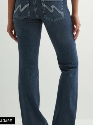 Blå bootcut jeans med kontrastsömmar - Snygga blå bootcut jeans med vita kontrastsömmar på bakfickorna och dubbla knappar fram. Jeansen har klassisk femficksdesign och är tillverkade i ett mjukt denimtyg som sitter skönt på kroppen.