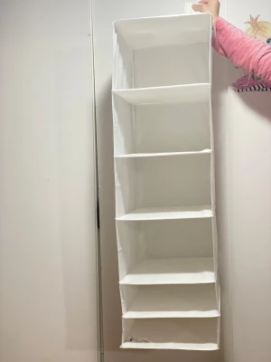 Vit hängande förvaringshylla tyg - Praktisk vit hängande förvaringshylla i tyg med fem rymliga fack. Perfekt att hänga för extra plats till kläder, skor eller accessoarer. 