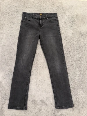 Mörkgrå Lee jeans straight fit - Säljer ett par mörkgrå jeans från Lee i rak modell. Klassisk femficksdesign med knapp och dragkedja framtill. Jeansen är tillverkade i ett mjukt bomullsmaterial och har en stilren look som passar till det mesta.