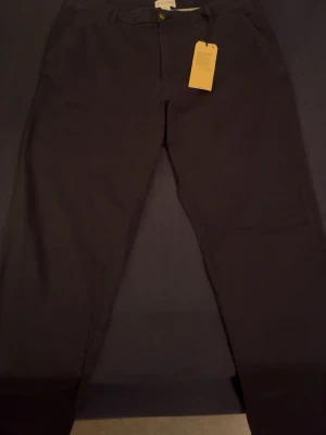 Svarta chinos från Holly & Whyte - Stilrena svarta chinos från Holly & Whyte by Lindex, modell Freja. Klassisk rak passform med hällor för bälte och diskreta fickor. Perfekta för en clean och enkel look. Tillverkade i mjuk bomull för skön känsla hela dagen.