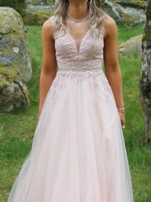 Balklänning ljusrosa med glitter - Elegant ljusrosa långklänning med spetsdetaljer med glitter upptill och v-ringning. Kjolen är i flera lager av tunt tyg och har en hög slits framtill. Perfekt för bal eller festliga tillfällen. Klänningen har ärmlös design och markerad midja. Köpt förra året på Kristina brud och fest i Jönköping. Nypris 4500 kr 