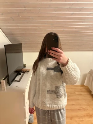 Vit chunky stickad tröja med mönster - Säljer en vit chunky stickad tröja med grafiskt mönster i grå och svart på framsidan. Tröjan har rund hals, långa ärmar och breda ribbade muddar vid ärmslut och nederkant. Perfekt för dig som gillar en oversized och mysig stil.
