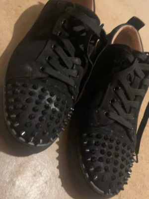 Loubs - Säljer ett par svarta loubs med coola svarta nitar över tån och snörning framtill. Skorna har en rund tå och är tillverkade i mocka-liknande material. Perfekta för dig som vill sticka ut lite extra. Använder inte dessa då dom är för små priset är dusketerbart