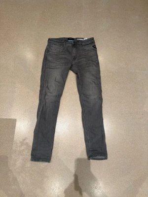 Replay Anbass grå jeans slim fit - Snygga grå jeans från Replay, modell Anbass. Slim fit med klassisk femficksdesign och diskreta detaljer. Jeansen är tillverkade i stretchig bomullsblandning för skön passform och har en modern look som passar till det mesta. Mycket bra skick byxorna är använda fåtal gånger.