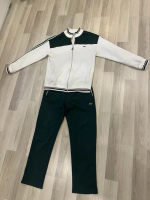 Mörkgröna mjukisbyxor från Lacoste - Mörkgröna mjukisbyxor från Lacoste med klassisk rak passform. Byxorna är i mjukt material och har resår i midjan. Perfekta för en avslappnad och sportig stil. Hög kvalite i storlek S