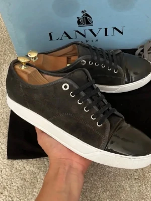 Bruna Lanvin sneakers i mocka och lack - Snygga bruna  sneakers från Lanvin med ovandel i mocka och lackad tå. Klassisk låg modell med vita sulor och svarta snören. Perfekta för dig som vill ha en stilren och exklusiv sneaker med unika materialval.  Kan gå ner i pris vid snabb affär, ingen box ingår 