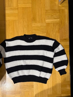 Svartvit randig stickad tröja - Säljer en oversized stickad tröja med breda svarta och vita ränder. Tröjan har rund halsringning, långa ärmar och ribbade muddar vid ärmslut och nederkant. Perfekt för en avslappnad och trendig look.