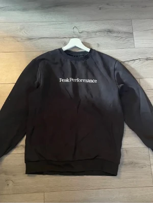 Svart sweatshirt Peak Performance M - Svart sweatshirt från Peak Performance med vit logotyp på bröstet. Klassisk rund halsringning och ribbade muddar vid ärmslut och nederkant. Perfekt för en avslappnad och stilren look. I mycket bra skick.