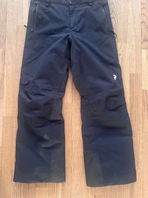 Svarta skidbyxor Peak Performance 150 - Säljer ett par svarta skidbyxor från Peak Performance i storlek 150. ( använda av en som är 160 lång) Byxorna har raka ben, dragkedjor vid fickorna och förstärkta partier vid bensluten. Mycket fint skick. Använt fåtal ggr. Nypris 1600kr