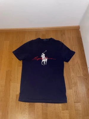 Ralph Lauren T-shirt - En Ralph Lauren T-shirt med riktigt snyggt tryck. Den är lite sliten nertill som ni ser men annars är allting bra. Skriv ifall ni har nån mer fråga!