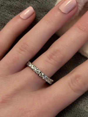 Silverfärgad ring med gnistrande stenar - Snygg silverfärgad ring med gnistrande, klara stenar runt hela bandet. Ringen har en klassisk och elegant design som verkligen fångar ljuset. Perfekt för dig som gillar stilrena accessoarer med lite extra bling.Vid köp av fler ringar kan jag slå ihop annonserna så frakten blir billigare.