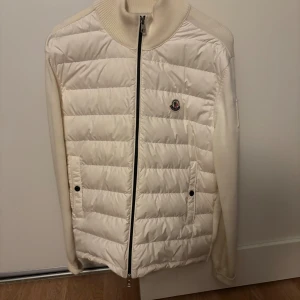 Vit pufferjacka från Moncler - Snygg vit pufferjacka från Moncler med quiltad front, ribbstickad krage och ärmar. Jackan har dragkedja framtill, två fickor med knappar och Moncler-logga på bröstet. Perfekt för dig som vill ha en clean och exklusiv look.