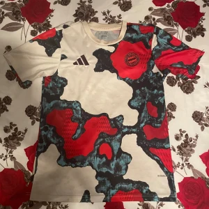 Bayern München Adidas fotbollströja - Unik Bayern München fotbollströja från Adidas med coolt abstrakt mönster i rött, svart och blått på beige botten. Kortärmad modell i lätt och ventilerande material, perfekt för match eller träning. Broderat klubbmärke och Adidas-logga på bröstet.