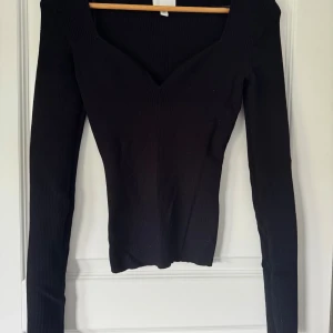 Svart ribbad långärmad topp H&M - Svart ribbad topp från H&M med lång ärm och snygg v-ringning. Modellen är figurnära och har en stretchig känsla som sitter riktigt snyggt. Perfekt att styla med jeans eller kjol för en clean look.
