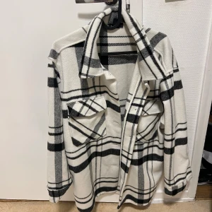 Rutig skjortjacka från Lindex i M - Snygg skjortjacka från Lindex i vitt och svart rutigt mönster. Jackan har klassisk krage, två stora bröstfickor med lock och knappar framtill. Perfekt lager-på-lager-plagg med lång ärm och avslappnad passform. Materialet är mjukt och känns fleece-liknande. Pris kan diskuteras!