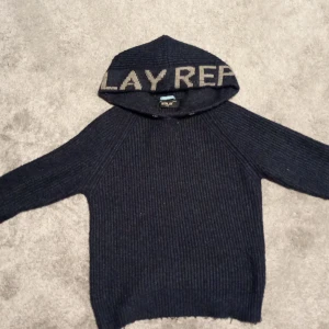 Mörkblå stickad hoodie från Replay - Mysig mörkblå stickad hoodie från Replay med ribbad struktur och stor huva där Replay-loggan syns tydligt. Långärmad modell som passar perfekt när det är kallt ute. Grym för dig som gillar en avslappnad och cool stil.