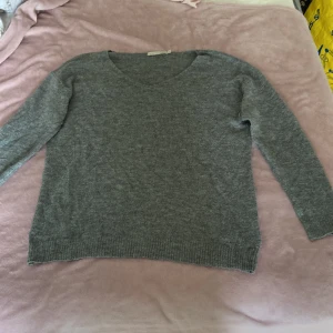 Grå stickad tröja från Lager 157 - Mysig grå stickad tröja från Lager 157 med v-ringad hals och långa ärmar. Perfekt för lager-på-lager och enkel att matcha med jeans eller kjol. Ribbstickade muddar vid ärmslut och nederkant ger en snygg finish.
