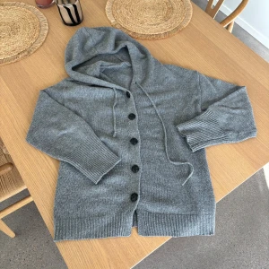 Grå stickad hoodie-kofta med knappar - Säljer min gråa stickade kofta som är i bra skick, den är köpt i Spanien för 1400kr. Passar perfekt nu till höst/vintern! Hör av er vid minsta fundering👌🏻
