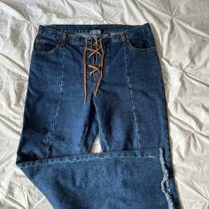 Blå jeans med snörning från Zoey Beth - Unika blå jeans från Zoey Beth med snygg snörning framtill istället för dragkedja. Jeansen har raka ben med rå kant nertill och klassiska bakfickor. Tillverkade i 100% bomull för en äkta denimkänsla.