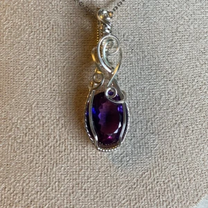 Silverhalsband med äkta lila/mörkblå safir  - Unikt halsband med en oval, facetterad lila/mörkblå safir infattad i snirkligt silver. Kedjan är tunn och diskret, medan hänget har en elegant och konstnärlig design med silvriga detaljer som ramar in stenen. Perfekt för dig som gillar färgstarka accessoarer med personlig touch. Septembers månadssten. Berlock: 600 Kedja: 50kr