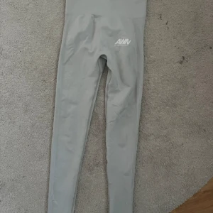 Grå leggings från Aware Nutrition - Snygga ljusgrå leggings från Aware Nutrition med hög midja och ribbade detaljer längs sidorna. Tight passform och stretchigt material som sitter skönt. Perfekta för gymmet eller chill dagar. Logga framtill på höften och scrunch-detalj bak.