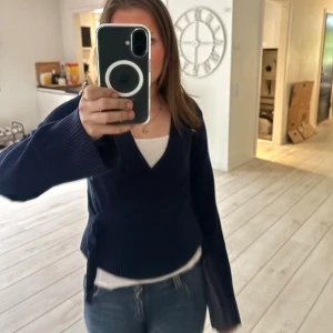 Mörkblå omlottstickad kofta - Mysig mörkblå omlottkofta med v-ringning och knyt i sidan. Stickad i ett mjukt material och har långa ärmar med lite vidare passform. Perfekt att slänga över ett linne eller t-shirt för en chill look.