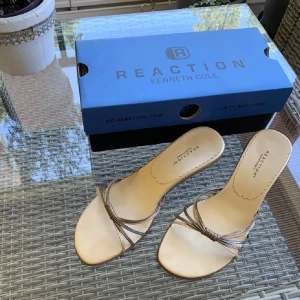 Guldfärgade sandaler från Kenneth Cole Reaction - Säljer ett par sandaler med remmar i guld, silver och brons från Kenneth Cole Reaction. De har  tunna remmar som korsar över foten och en liten knutdetalj framtill. 