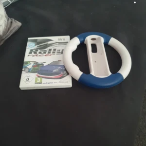 Rally Racer Wii + Ratt - Säljer Rally Racer till Nintendo Wii inklusive original ratt-tillbehör. Spelet och ratten är i gott skick med endast mindre tecken på användning. Perfekt för dig som vill ha en rolig racingupplevelse hemma! Fungerar med Wii-konsol.