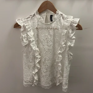 Vit spetsblus med volang från H&M Divided - Supersöt vit blus i spets från H&M Divided. Blusen är ärmlös med volangdetaljer längs axlarna och har ett vackert blommigt spetsmönster. Rund halsringning och knapp i nacken för en extra fin touch. Perfekt för dig som gillar romantisk och feminin stil.🥰🥰