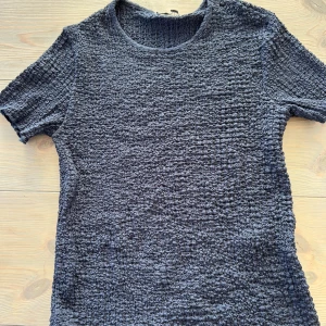 Mörkgrå ribbad t-shirt från Zara - Säljer en mörkgrå t-shirt från Zara i storlek S. T-shirten har korta ärmar och är tillverkad i ett ribbat, strukturerat material som ger en cool och unik look. Perfekt för dig som gillar stilrena basplagg med det lilla extra.
