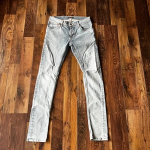Ljusblå från Nudie Jeans - Säljer ett par ljusblå skinny jeans från Nudie Jeans med klassiska orange sömmar och vågig brodyr på bakfickan. Jeansen har fem fickor, normal passform i midjan och är tillverkade i mjukt bomullsjeansmaterial. Perfekta för en avslappnad och stilren look. Aldrig använda 