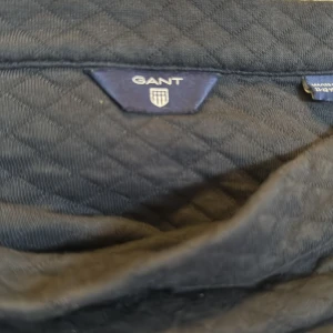 Mörkblå quiltad kjol från Gant - Supersnygg mörkblå kortkjol från Gant med quiltad struktur. Kjolen har dragkedja och knapp i sidan för enkel påklädning. Perfekt för dig som gillar klassisk och stilren look med en twist. Passar till många olika outfits!