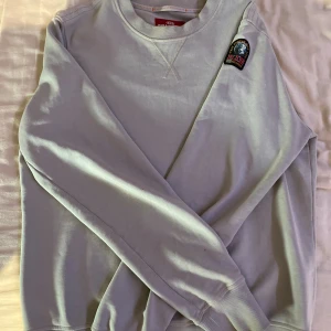 Ljusgrå fleece-tröja Parajumpers M - Ljusgrå fleece-tröja från Parajumpers i storlek M. Tröjan har rund hals, ribbade muddar och ett snyggt PJS-märke på axeln. Perfekt för dig som gillar stilrena och bekväma plagg med cool detalj. Fleece-materialet gör den extra mjuk och skön.