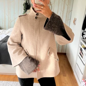 Beige ullkappa från Zara Woman XS - Säljer en beige jacka/cape från Zara i ullblandning. Jackan har hög krage, knappar och dragkedja framtill samt fickor med lock. Superfin att ha över tjocktröjor nu i höst!🥰🥰🥰 fint skick! Skicka till mig om prisförslag 
