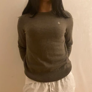 Brun tröja med broderad detalj - Mysig brun tröja med rund halsringning och lång ärm. Tröjan har en liten broderad detalj på bröstet och ribbade muddar vid ärmslut och nederkant. Perfekt för lager-på-lager under kyliga dagar.