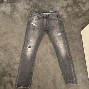 Replay Rocco grå slitna jeans - Snygga Replay Rocco jeans i grå tvätt med slitningar och trasiga detaljer på benen. Klassisk femficksmodell med komfort fit och raka ben. Storlek W30,L32. Jag har använt dessa jeans i en månad ish. 